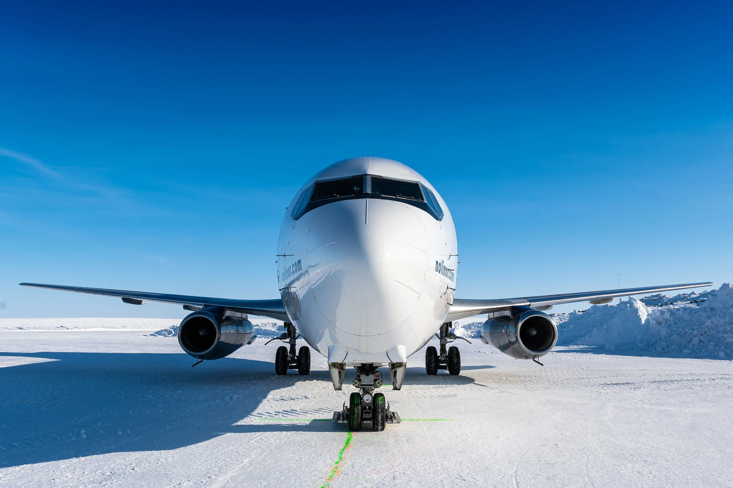 A commercial airplane is parked on a snowy runway under a clear blue sky, showcasing its front view and landing gear.