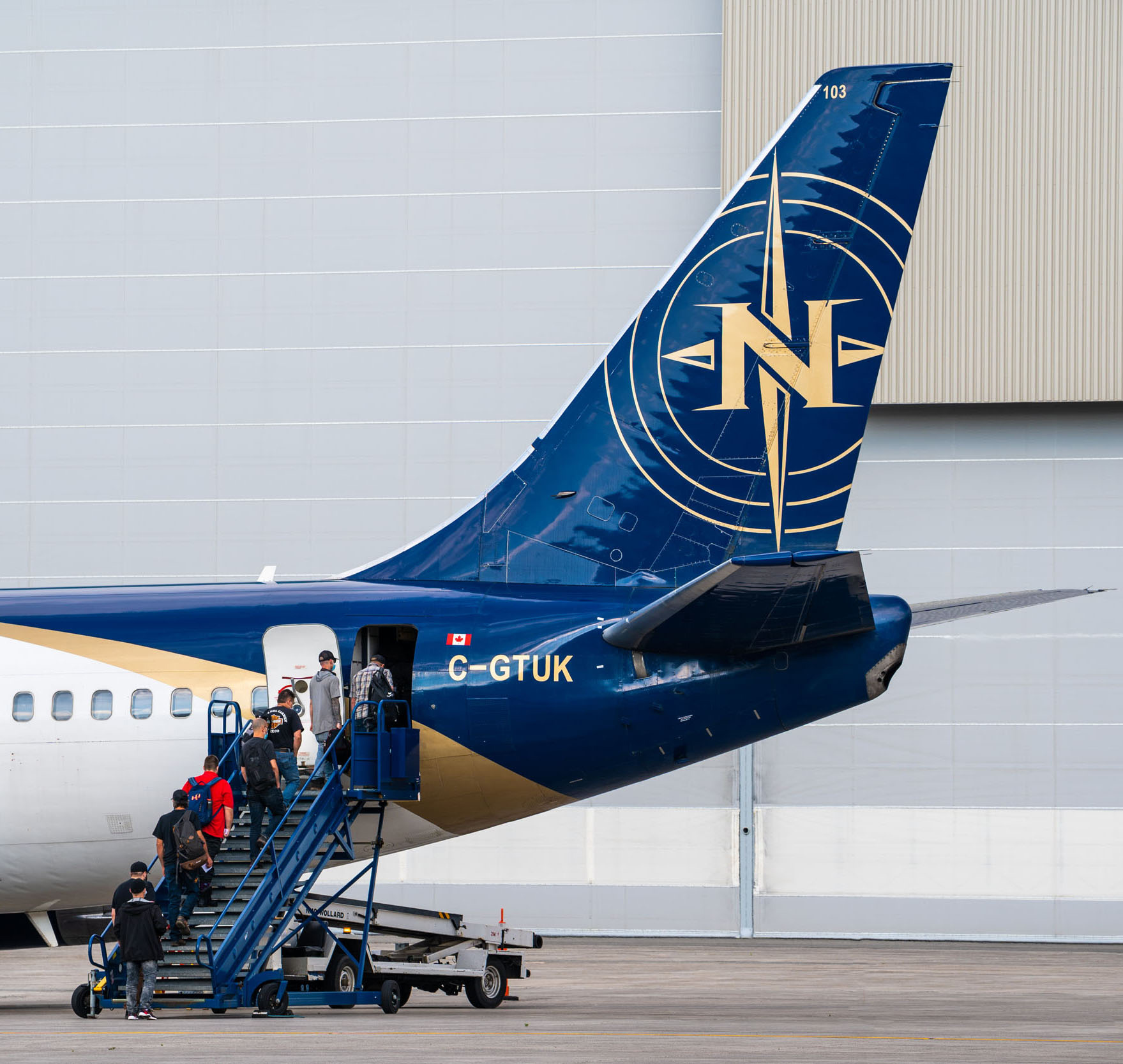 Passengers board a blue and gold aircraft with the registration C-GTUK, using a stairway at the airport.