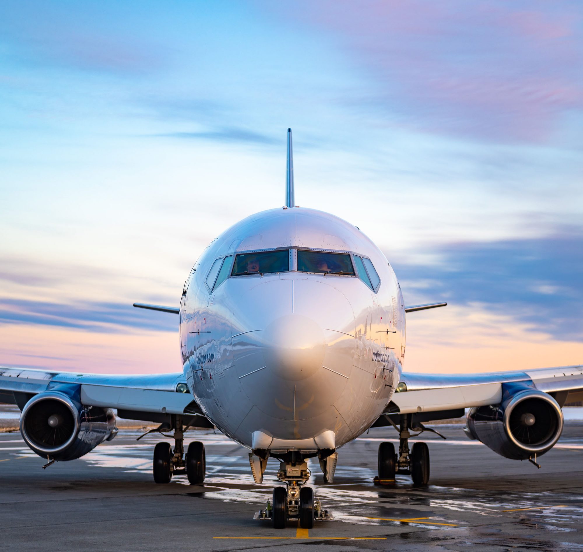 A commercial airplane is parked on the tarmac, facing the camera, with a colorful sunset sky in the background.