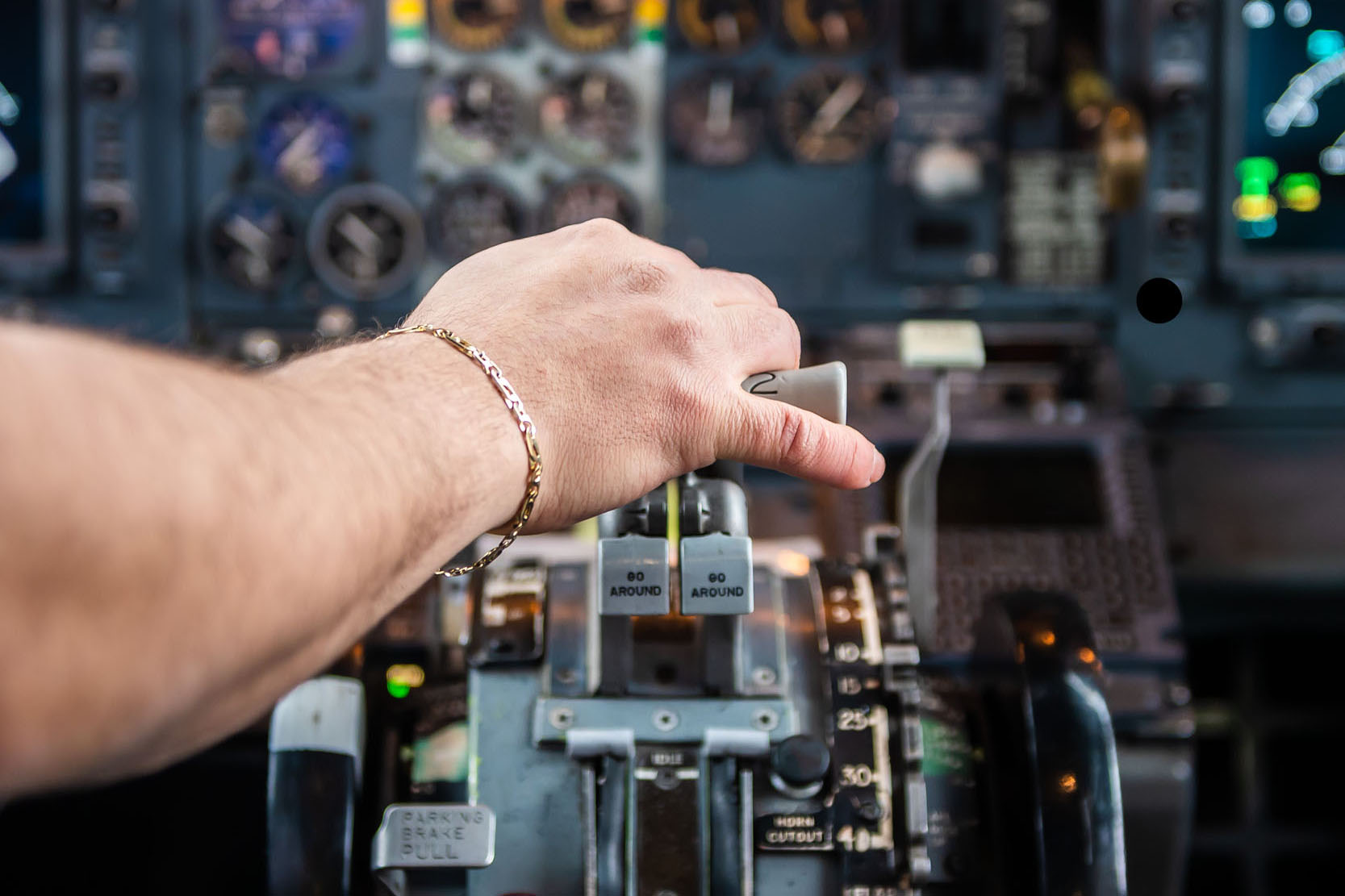 A hand adjusts the throttle lever in an aircraft cockpit, surrounded by various control panels and instruments.