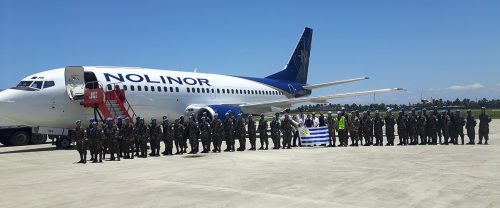 A group of soldiers stands in formation on an airstrip, with a Nolinor airplane in the background and a flag displayed.