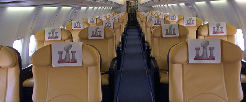 Cabine d'un avion avec des sièges en cuir beige, ornés de serviettes portant le logo du Super Bowl, ambiance sportive.