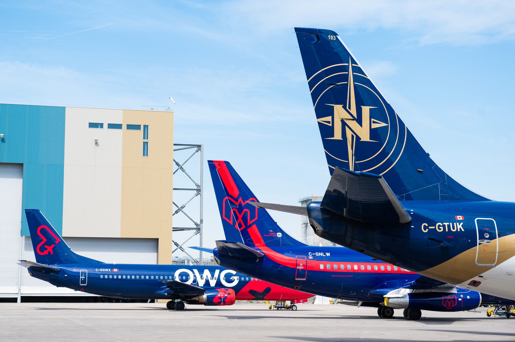 Two airplanes parked at an airport, one featuring a red and blue design with "OWG" on the tail, the other in dark blue with a logo.