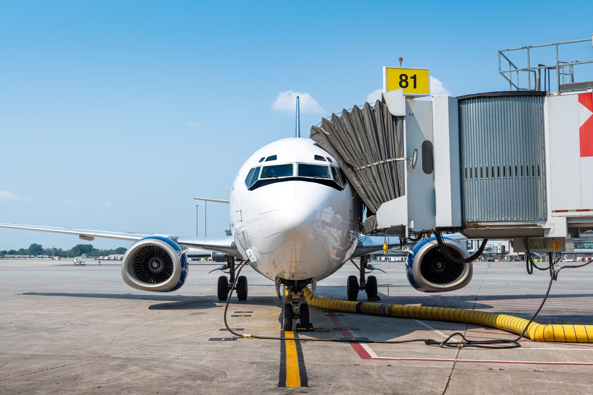 Un avion de ligne est garé à un terminal, relié à une passerelle. Le ciel est dégagé et le sol est en béton.