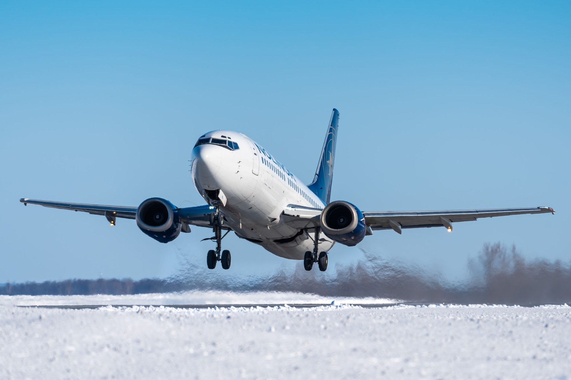A commercial airplane takes off from a snowy runway, with clear blue skies in the background.