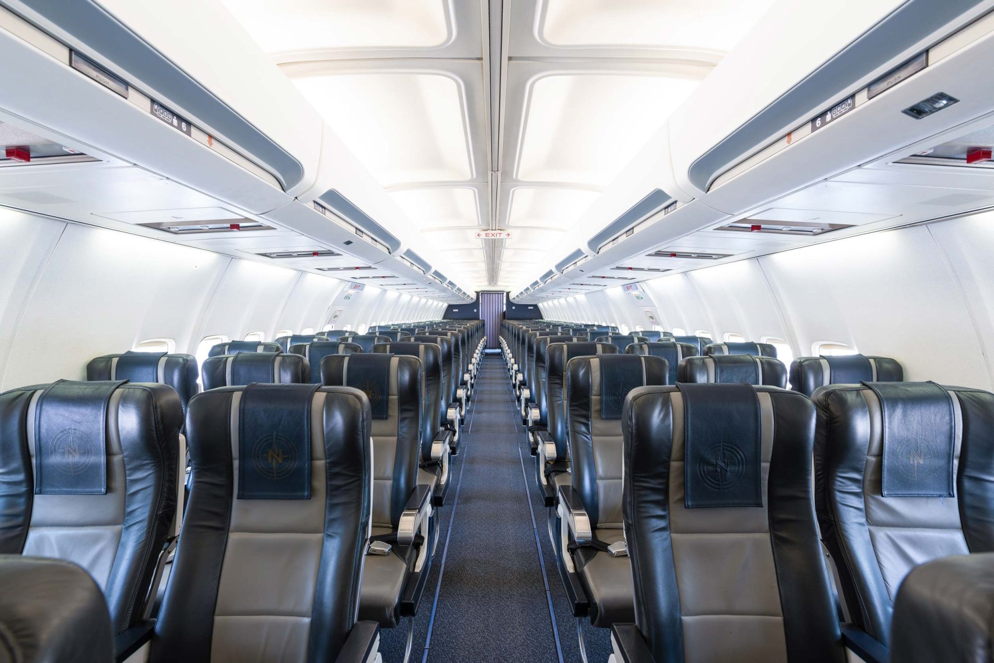 Empty airplane cabin featuring rows of black leather seats, with overhead compartments and soft lighting illuminating the aisle.