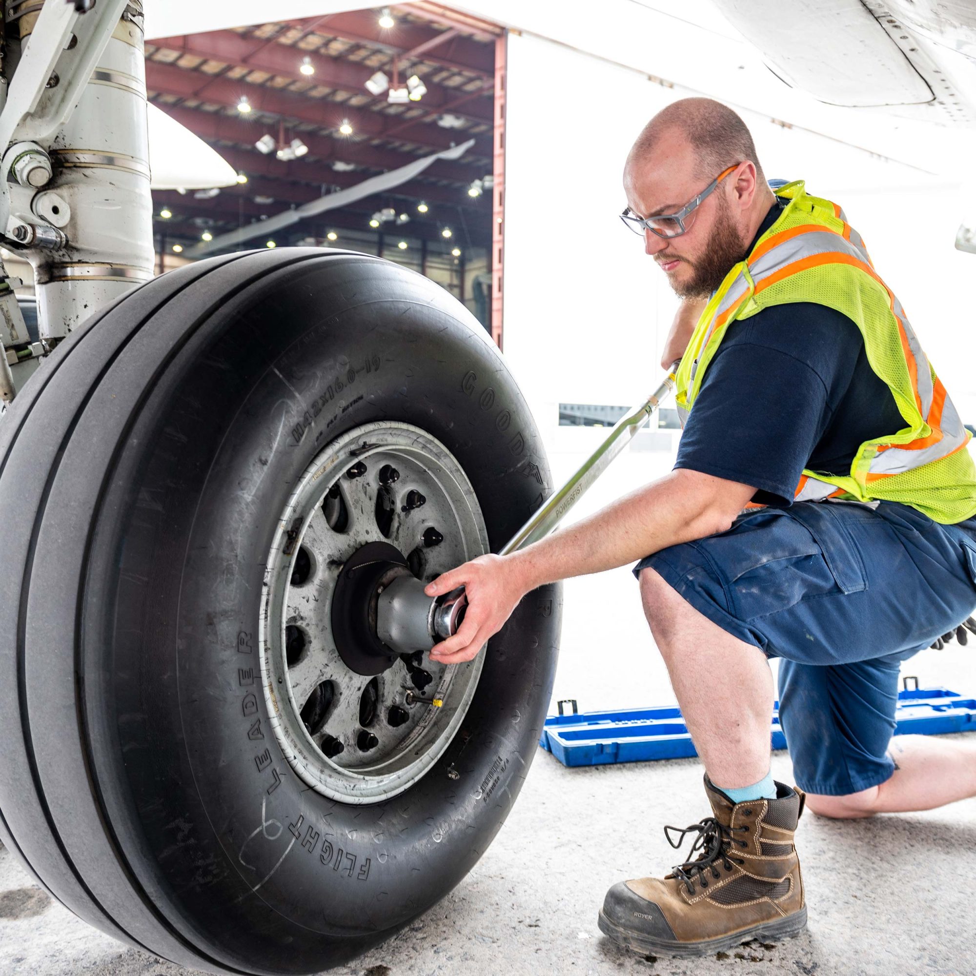 Un technicien en gilet de sécurité effectue une maintenance sur la roue d'un avion, utilisant une clé à molette pour ajuster l'écrou.