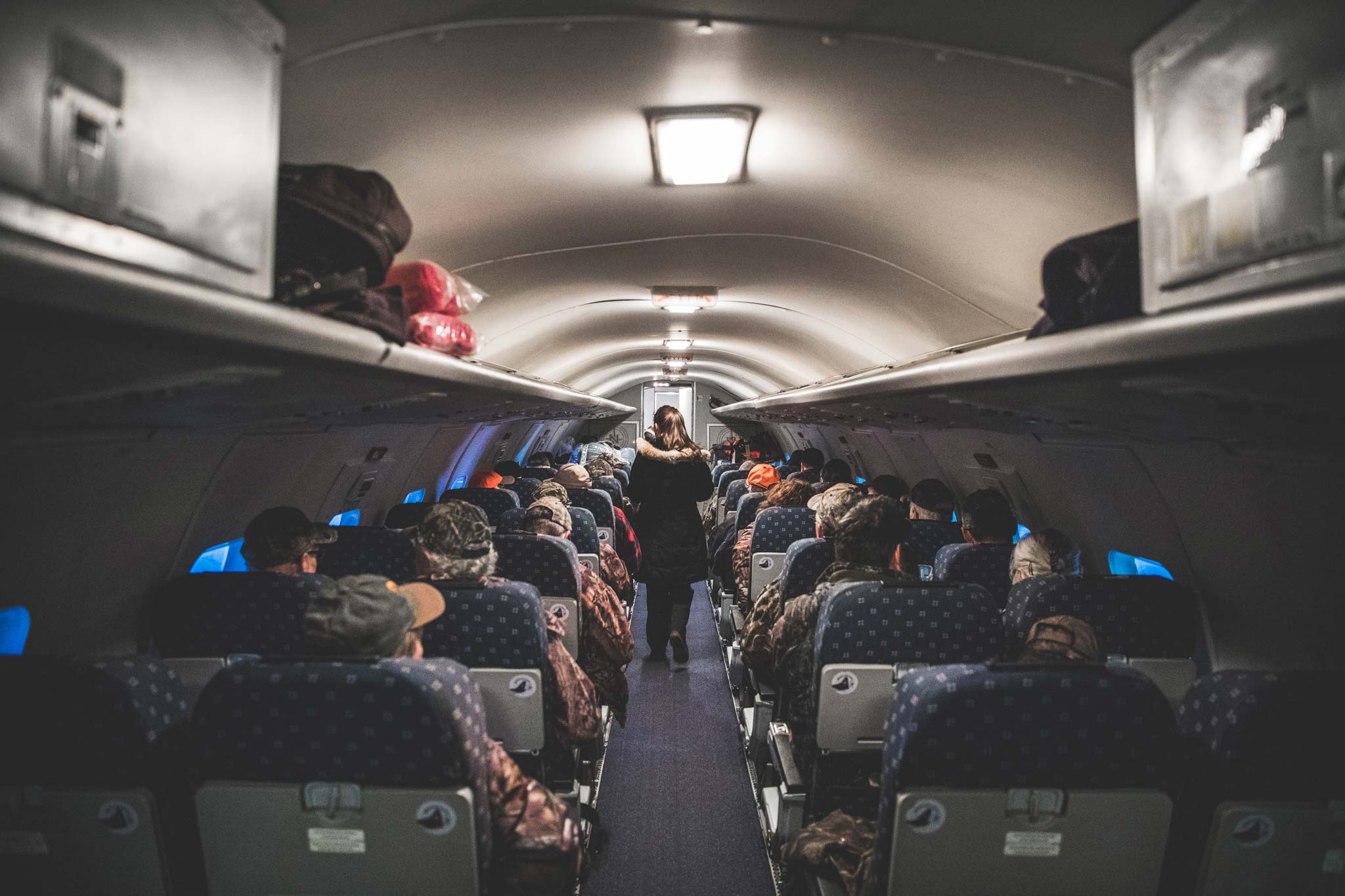 Passengers in camouflage clothing sit in an airplane aisle as a flight attendant walks toward the front.