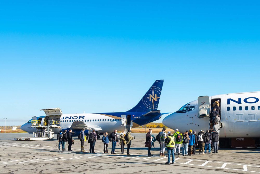 Des passagers descendent d'un avion sur le tarmac, tandis qu'un autre avion est stationné à proximité sous un ciel bleu clair.