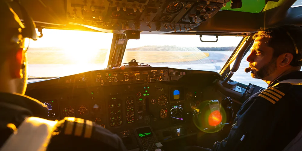 Deux pilotes dans le cockpit d'un avion, le soleil levant éclaire les instruments et les visages, créant une ambiance chaleureuse.
