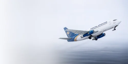 Un avion de la compagnie Nolinor décolle dans un ciel nuageux, montrant son design distinctif en bleu et blanc.