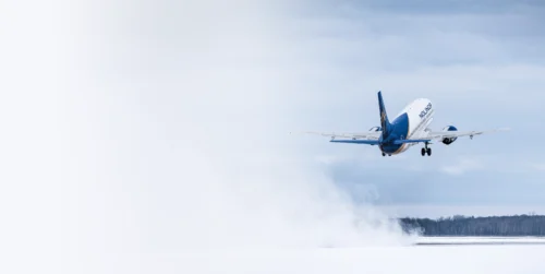 A Nolinor airplane takes off against a cloudy sky, leaving a trail of mist behind as it ascends.
