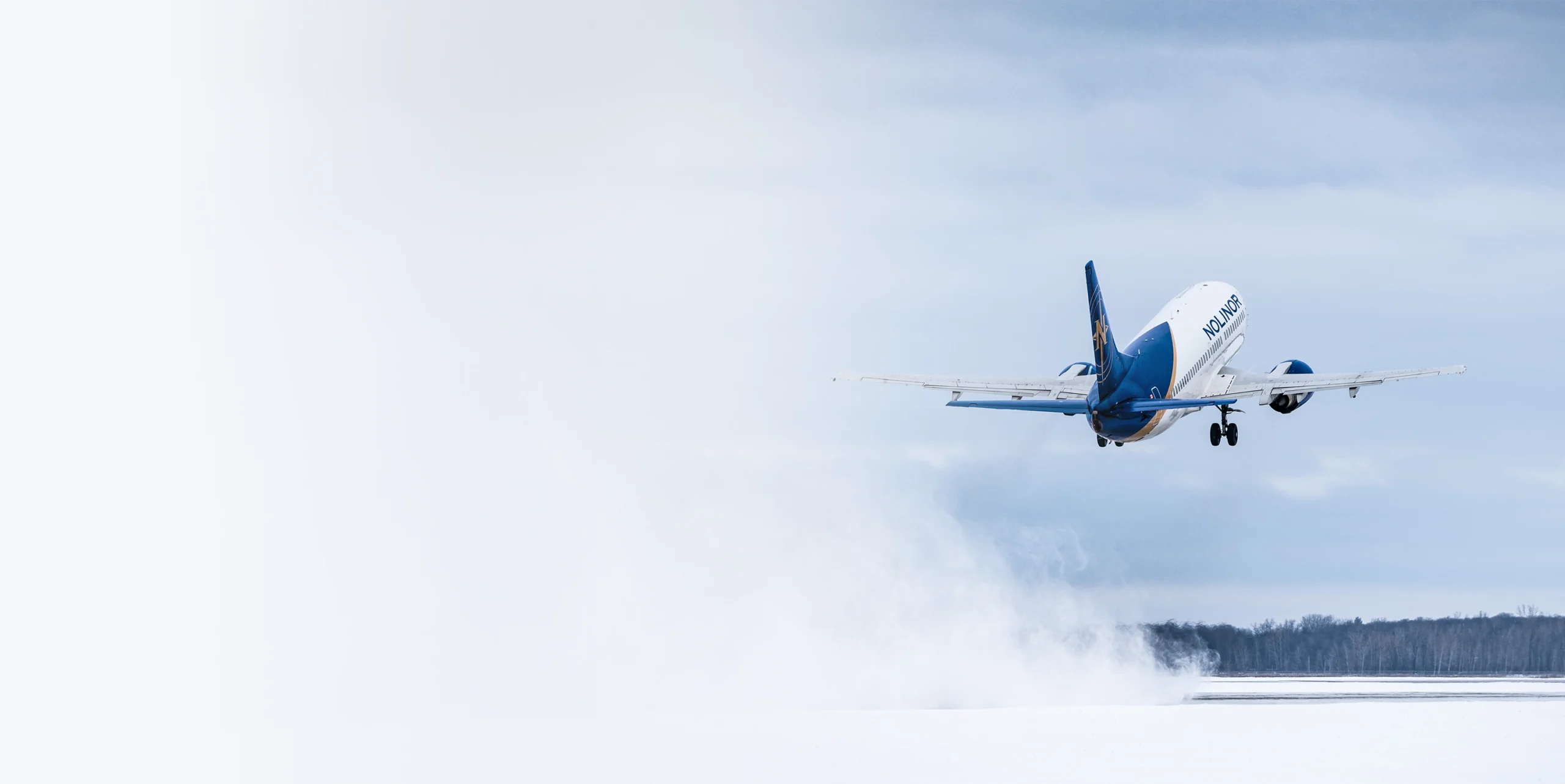 Un avion décolle, incliné vers la droite, sur fond de ciel nuageux et de brume. L'appareil est aux couleurs d'une compagnie aérienne.