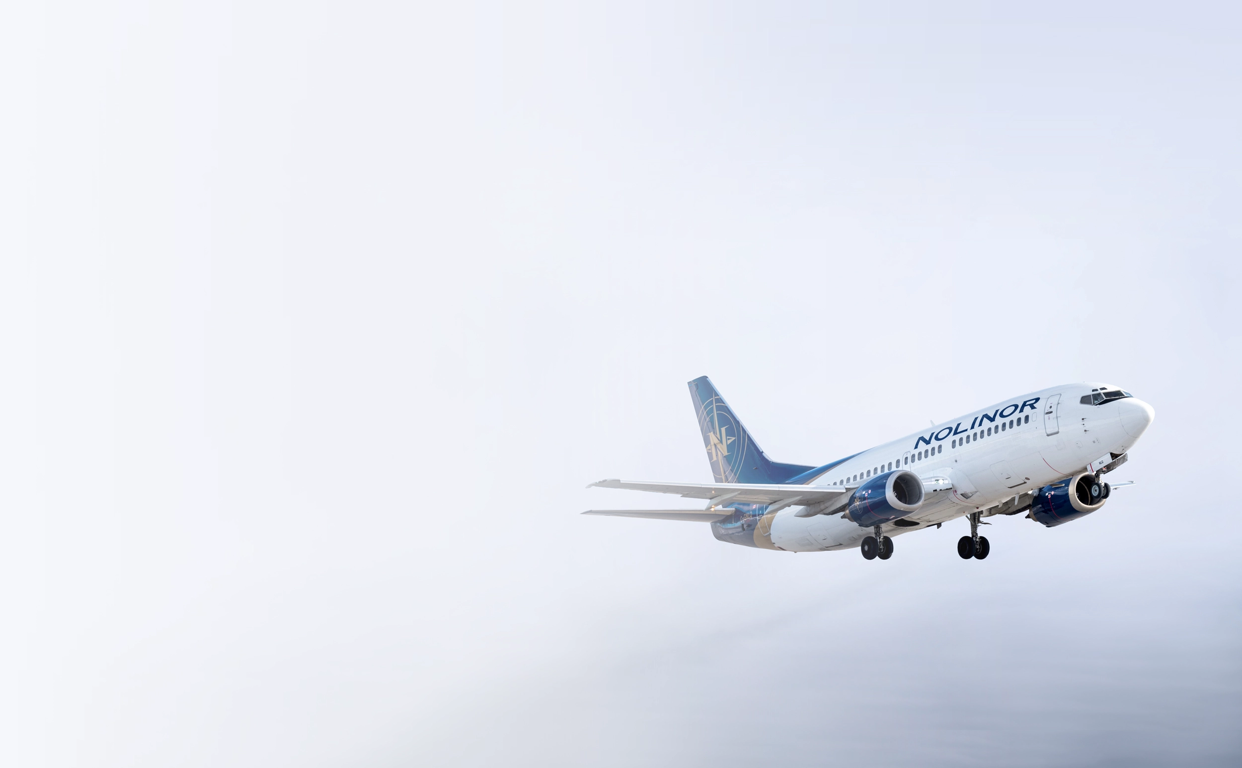 A Nolinor aircraft landing, with cloudy skies in the background.