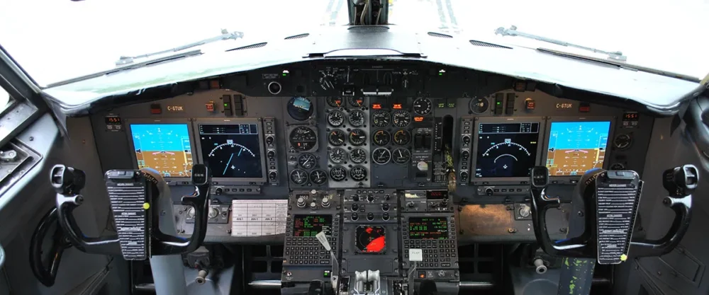 Cockpit view of an aircraft featuring multiple digital displays, control panels, and joystick controls for navigation and operation.