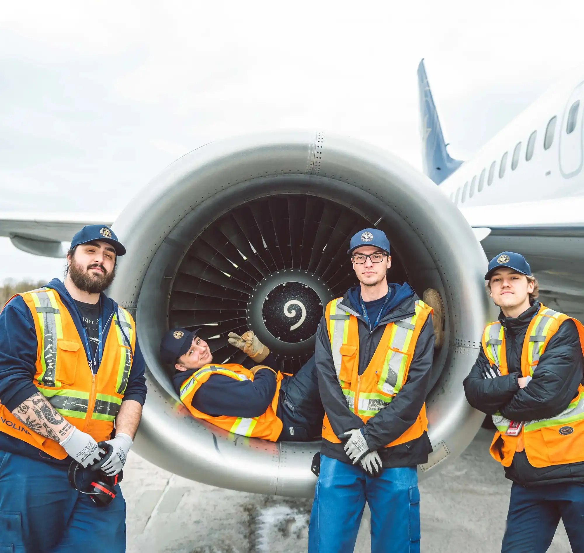 Four airport workers in safety vests pose near a jet engine, showcasing teamwork and aviation maintenance.