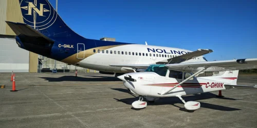 Un petit avion Cessna blanc et rouge est garé devant un grand avion commercial aux couleurs de Nolinor, sous un ciel bleu.