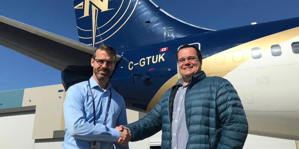 Two men shake hands in front of a blue and gold aircraft, with the registration number C-GTUK visible on the tail.