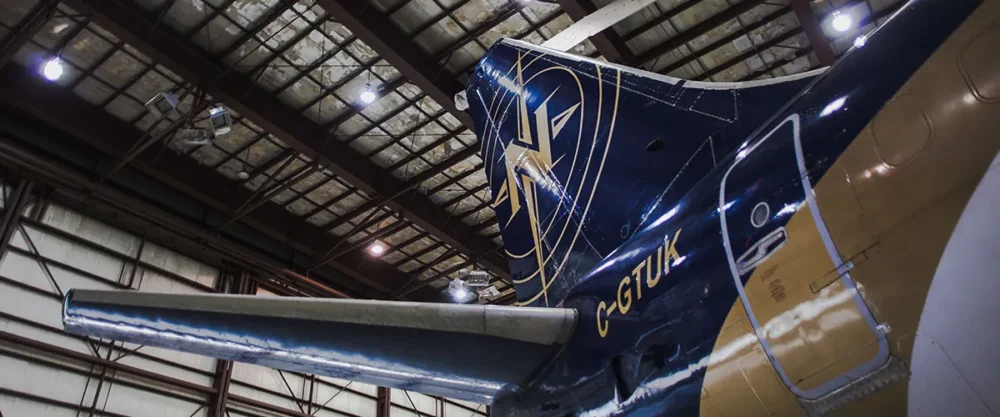 Tail section of a vintage aircraft inside a hangar, showcasing a blue and gold design with a logo and wing detail.