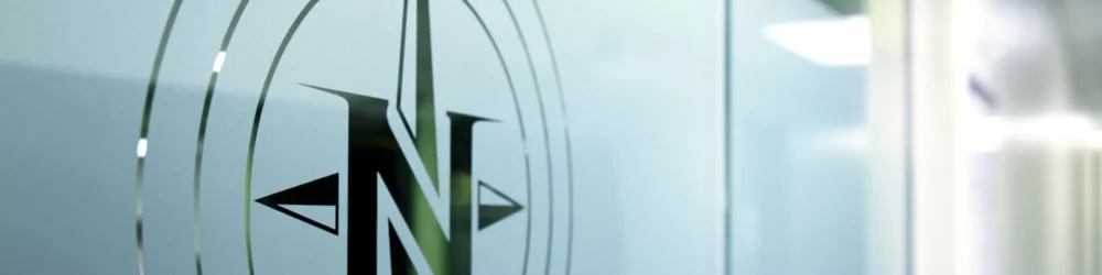 Frosted glass featuring a stylized compass design with a prominent 'N' indicating north, set against a blurred background.