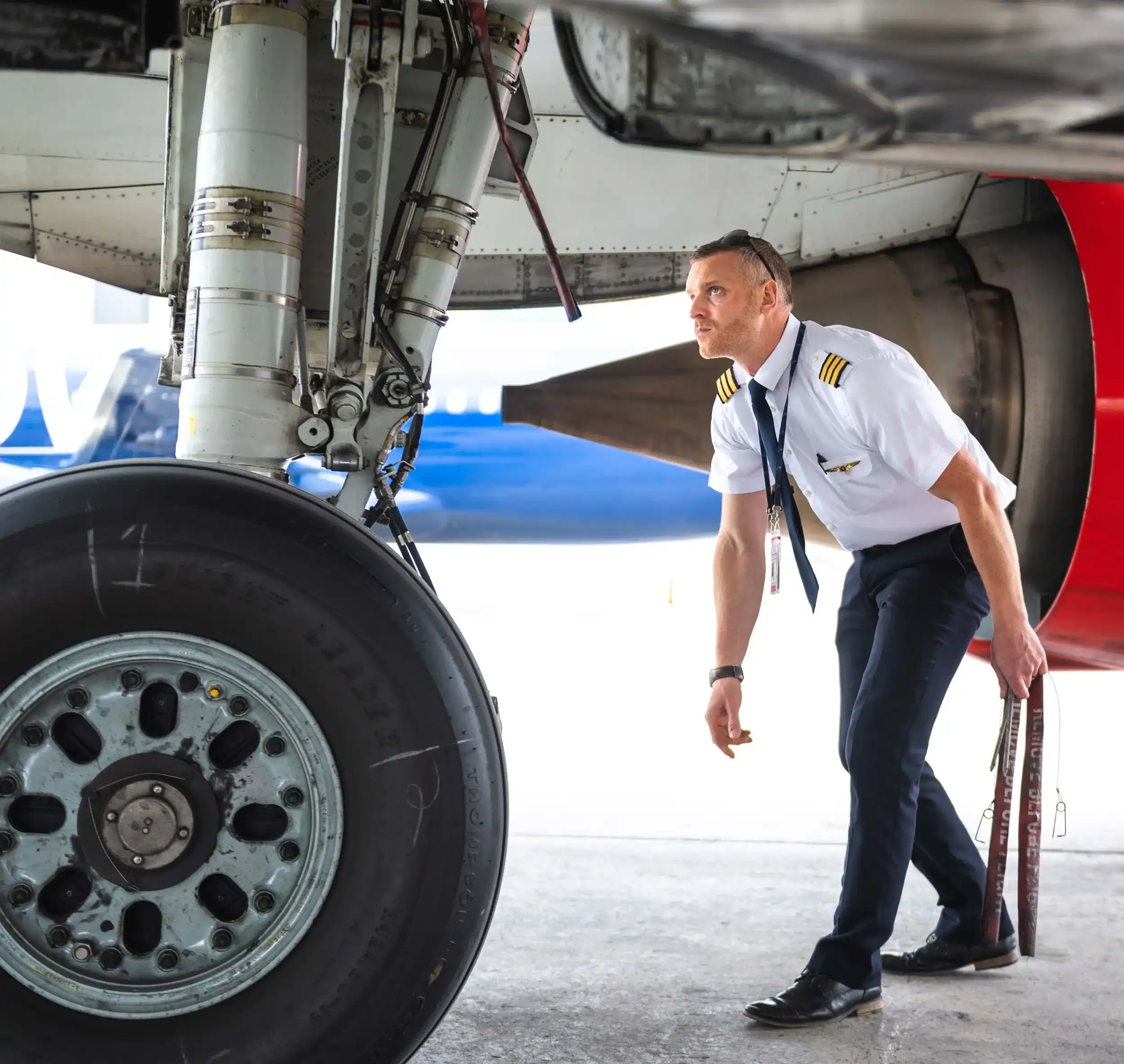 A pilot inspects an airplane's landing gear, focusing on the technical details before the flight. The setting is an airport.