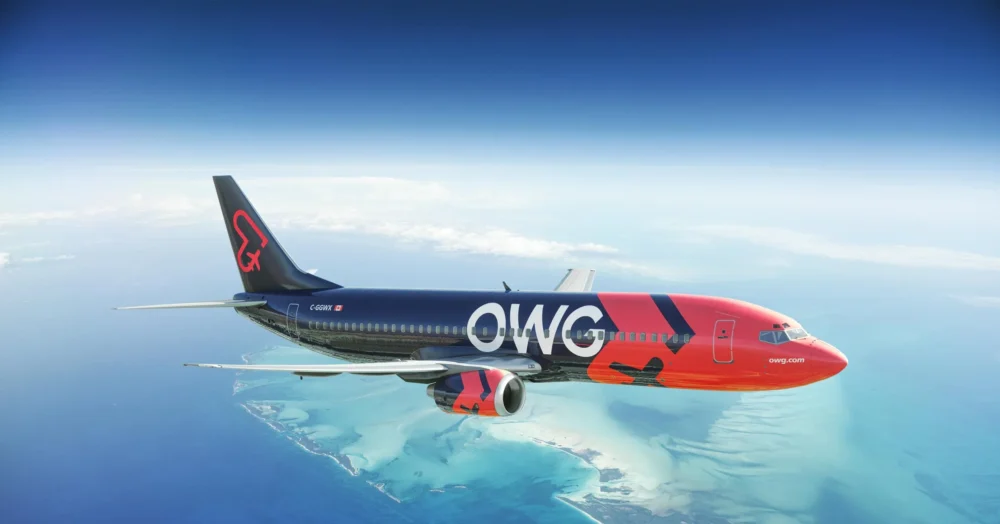 A colorful OWG airplane flies over a turquoise ocean and sandy islands, showcasing its vibrant branding against a clear sky.