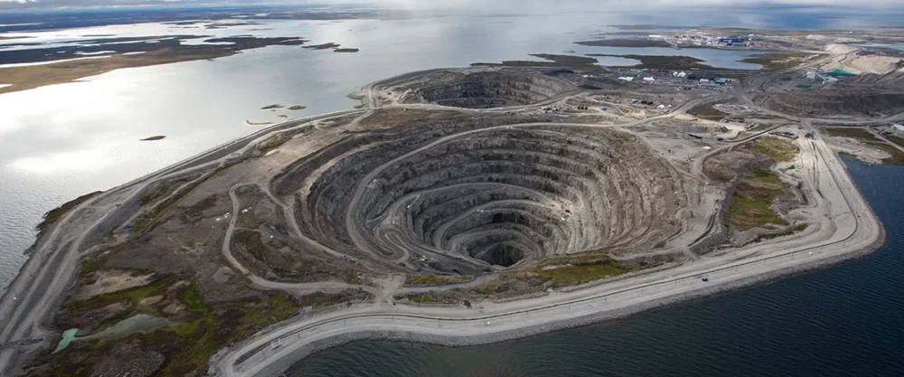 Aerial view of a large open-pit diamond mine surrounded by water, showcasing layered excavation and surrounding landscape.