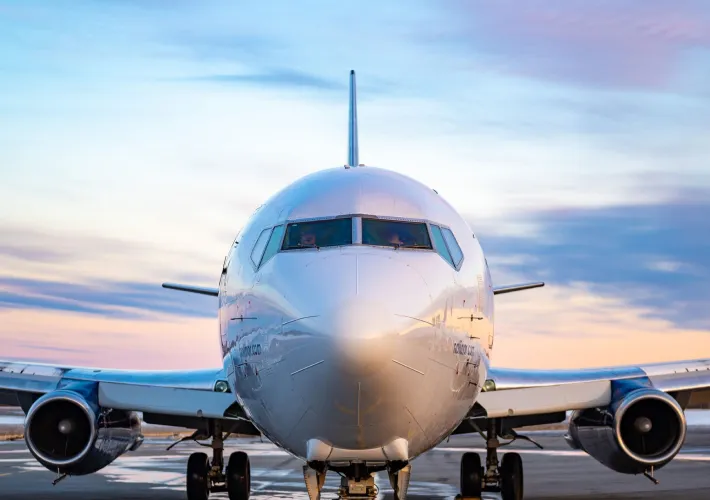 Un avion de ligne se trouve sur la piste, face à la caméra, sous un ciel coloré au lever du soleil. Les pilotes sont visibles à l'intérieur.