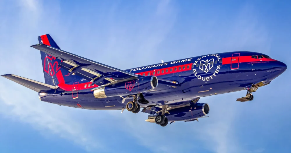 A blue and red airplane with "Toujours Game" and "Montreal" branding descends against a clear sky.