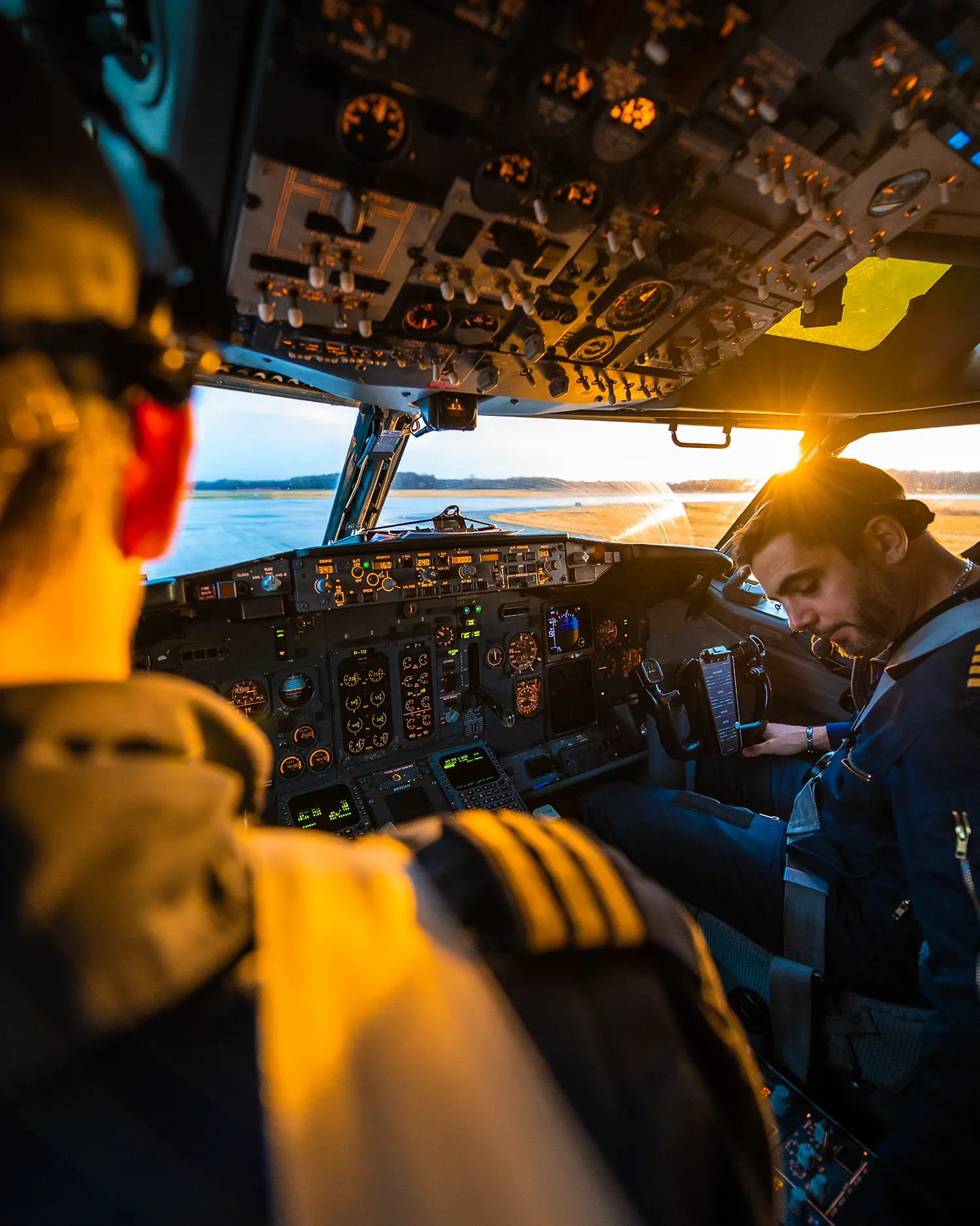 Deux pilotes effectuant leurs vérifications dans le poste de pilotage d'un Boeing 737 au lever du soleil.